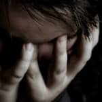 a child in the dark clutches their face with their hands in anguish
